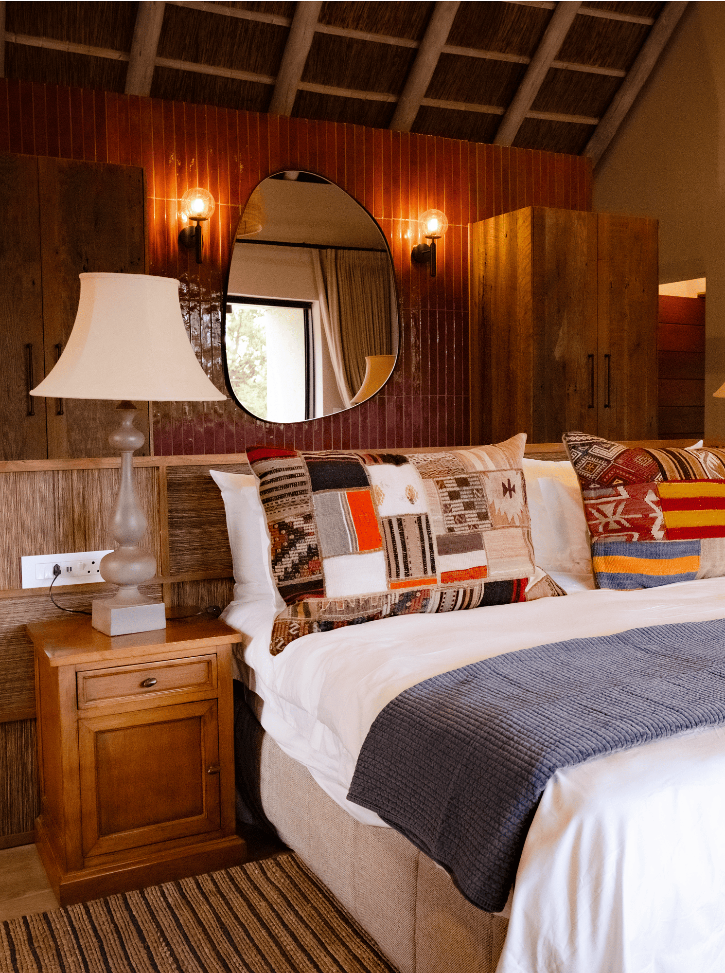 Stay with a Cozy bedroom with a rustic wooden headboard, patterned pillows, and a bedside lamp.