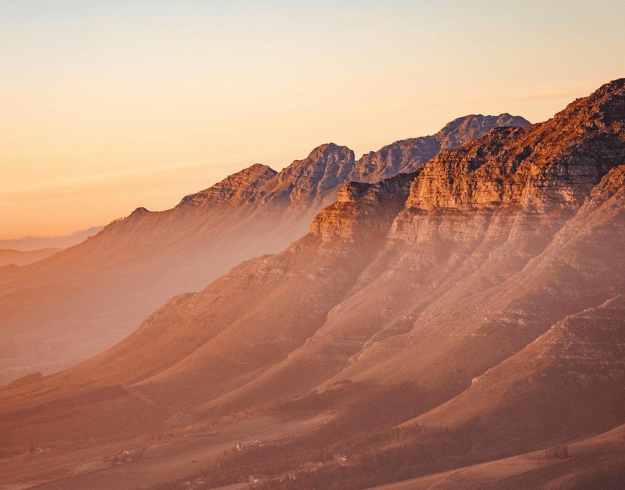 Golden hour sunset over rugged mountain range, casting long shadows.