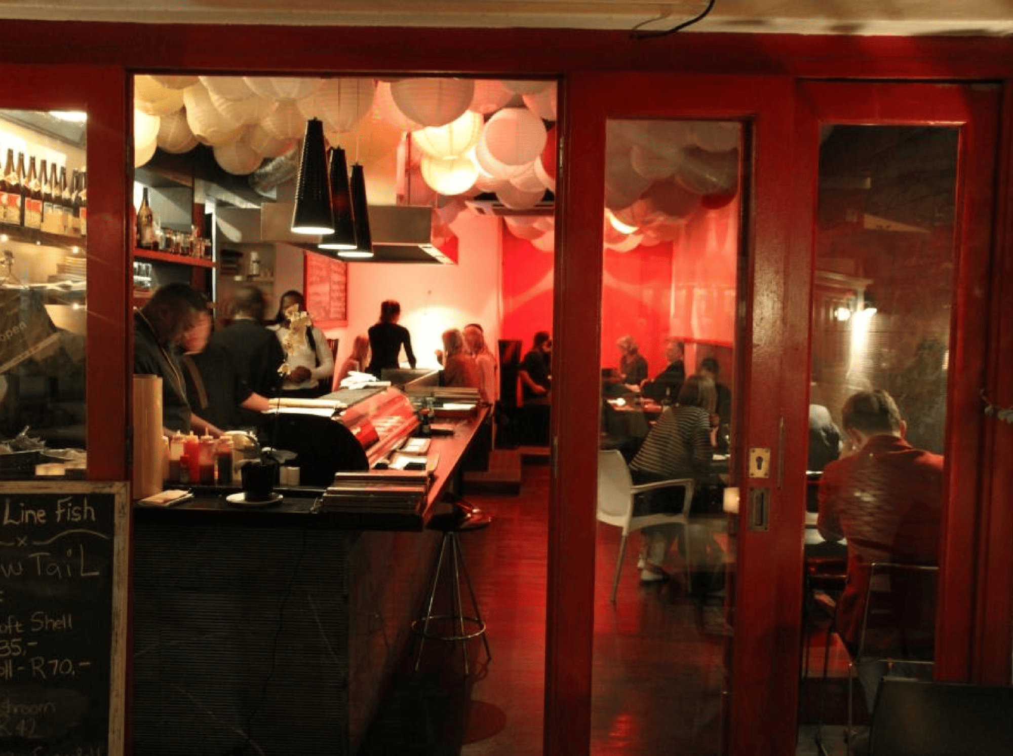 Interior of a Japanese restaurant with red accents, diners, and sushi bar, seen as you explore the Cape Winelands