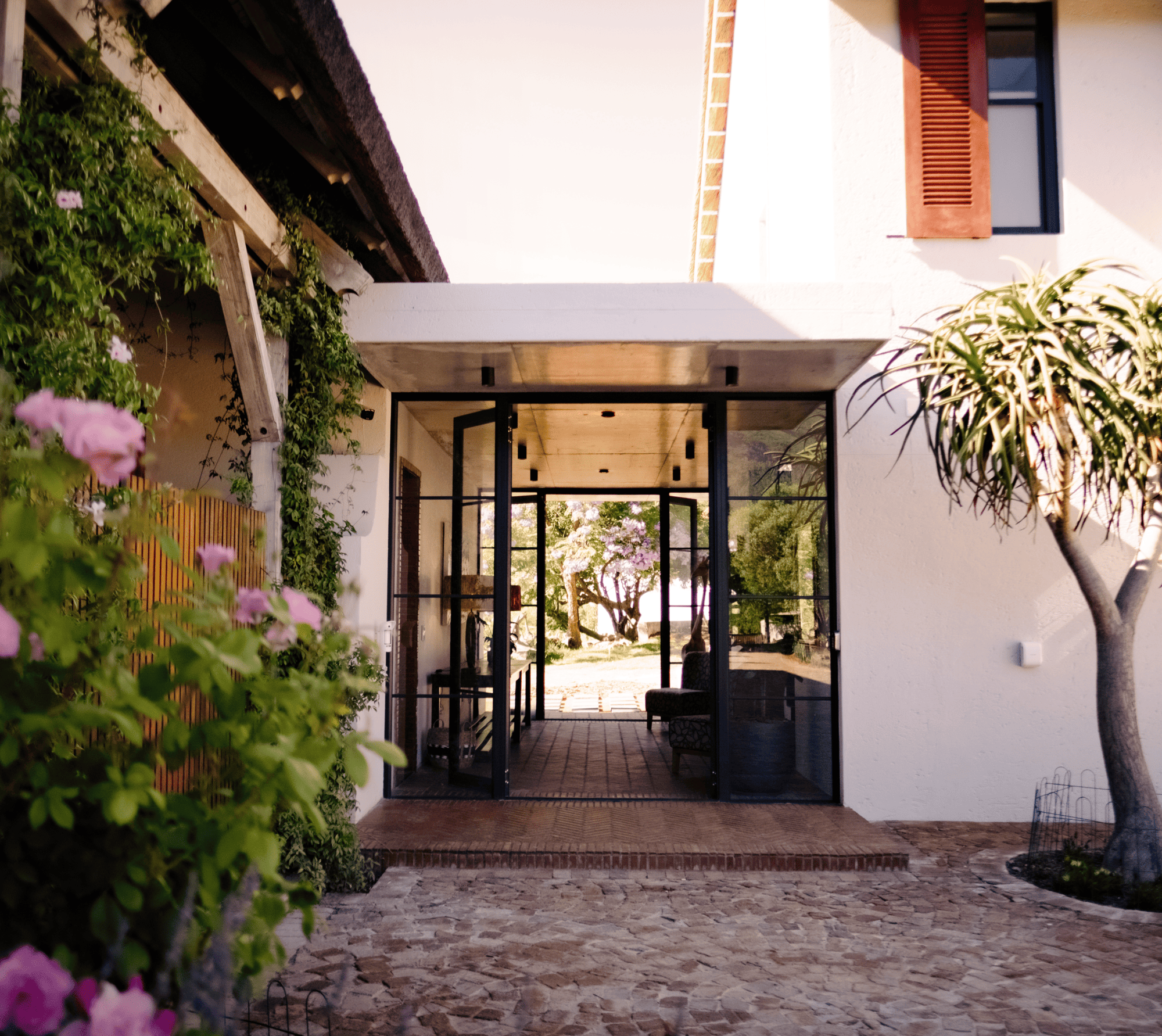 Modern home entrance with glass doors, lush greenery, and a paved walkway.