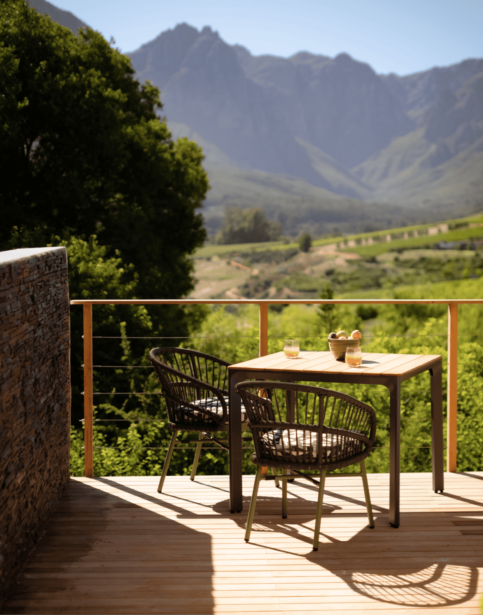 Outdoor dining table and chairs on a wooden deck with a mountain vineyard view