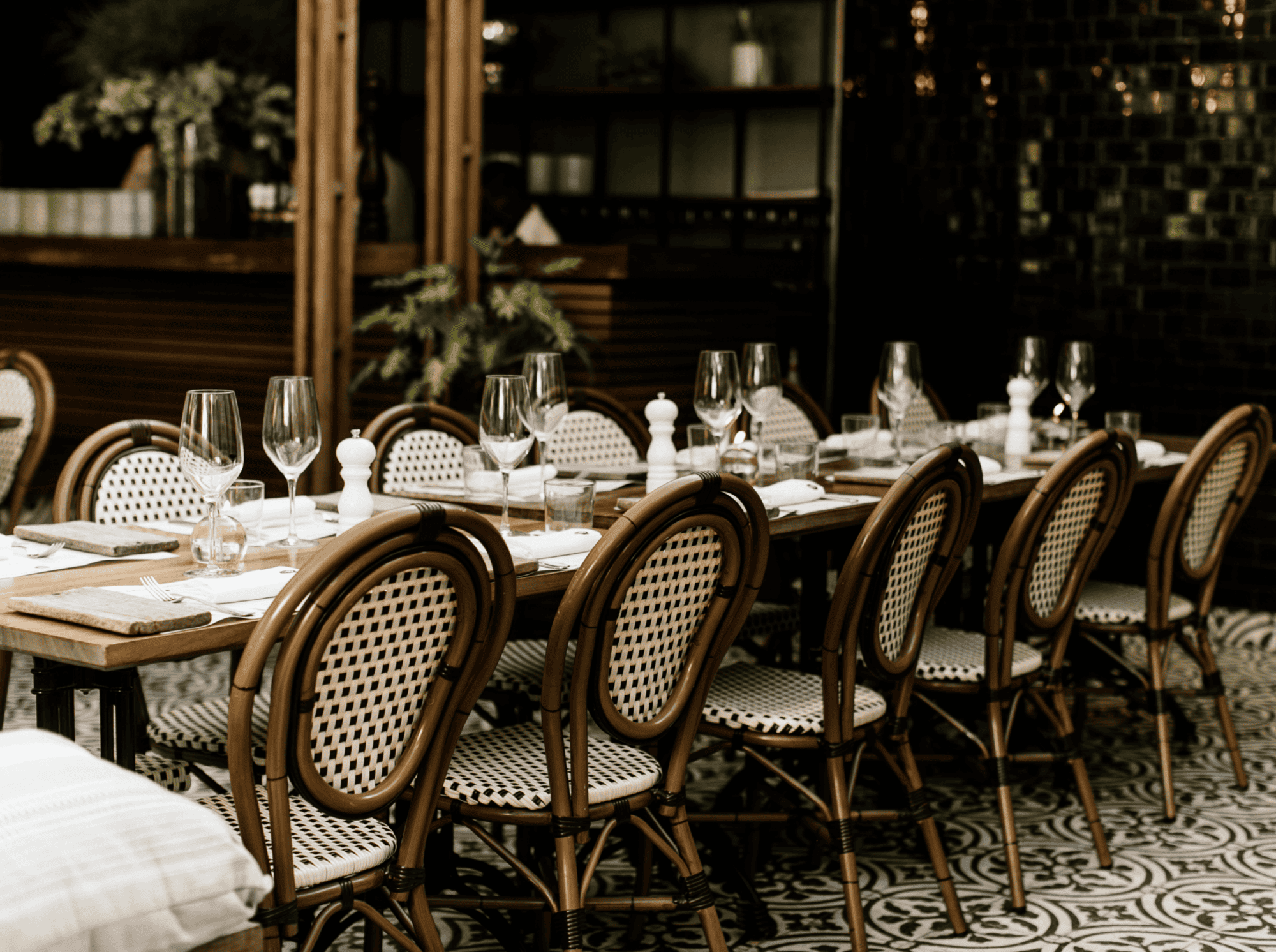 Elegant outdoor dining setup with rattan chairs and a long table set for a meal.
