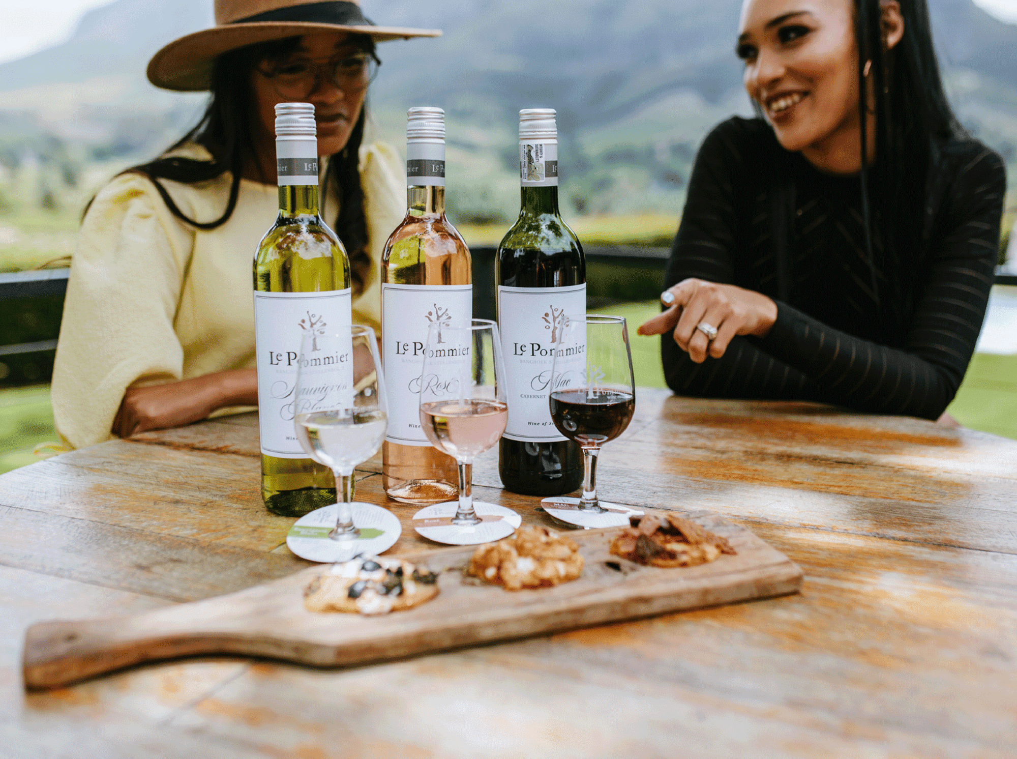 Two women enjoy Le Pommier wine and snacks outdoors.